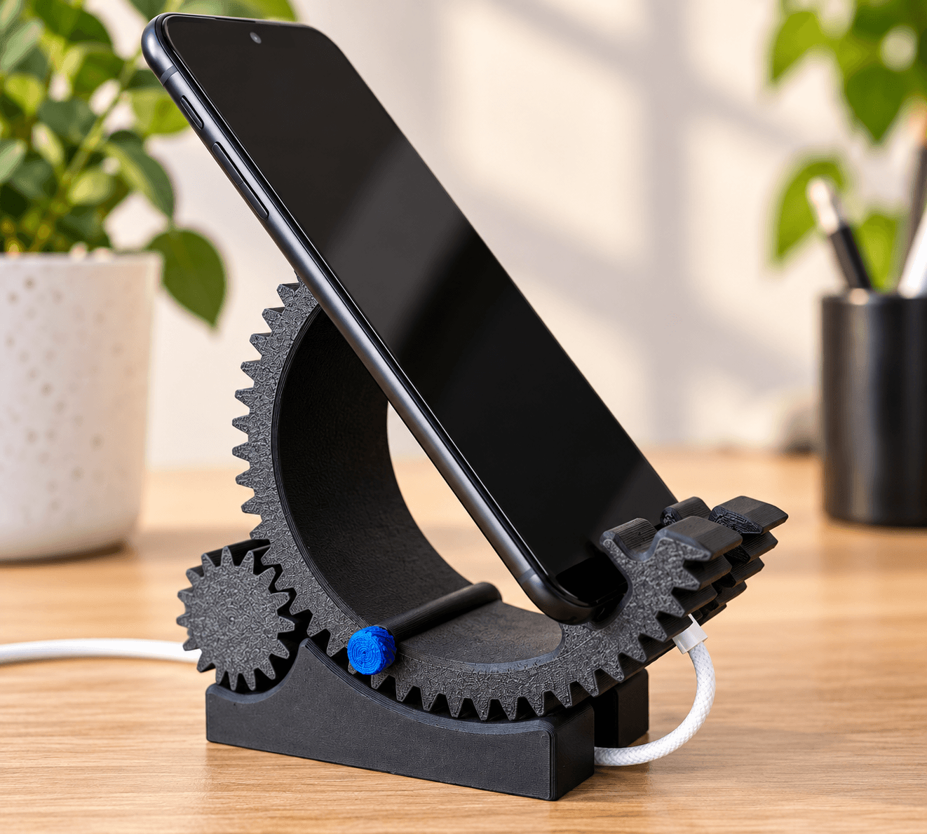 Black 3D printed adjustable gear-style phone stand holding a smartphone
